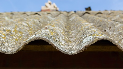 Roofing materials covered in flaky green and white asbestos dust.