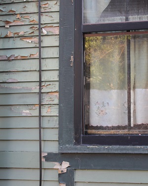 A home with peeling exterior siding and a damaged window frame.