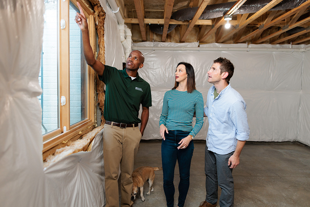 An NPI inspector takes two clients on a home walkthrough and points out a detail on the window sill.