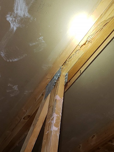 An interior view of a home shows a damaged wooden truss lit up by a flashlight beam.