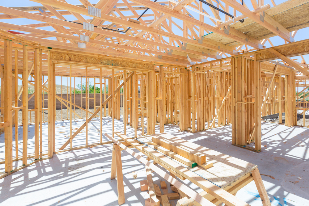 A new home is under construction with roofs and walls framed and building materials laying on the foundation.