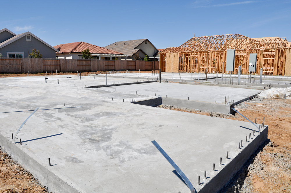 Two new homes under construction, one with its foundation poured, and the other at the framing stage.