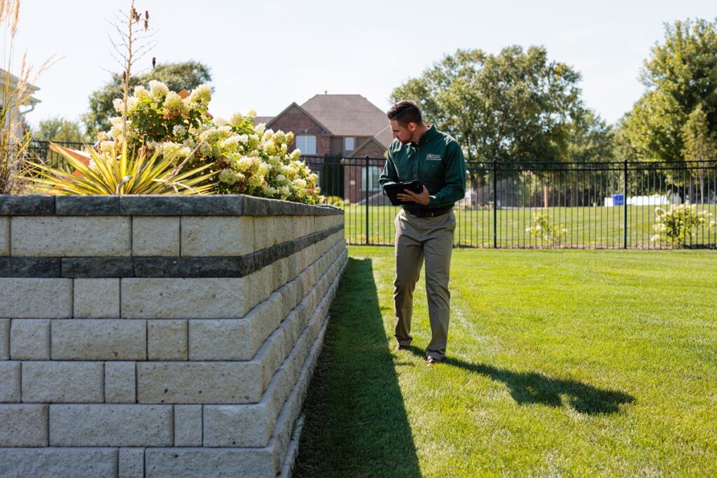 An NPI inspector walks along a retaining wall outside while holding his tablet.