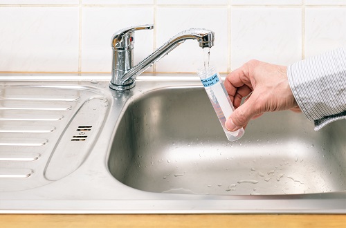 A vial is filled with water from a faucet for water testing.